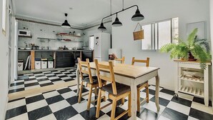 A kitchen with a checkered floor, wooden dining table, and chairs. There are black pendant lights, a refrigerator, and a microwave. - Casita Lucero (Málaga)