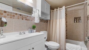 Een moderne badkamer met een witte wastafel, toilet, badkuip en douchegordijn.
