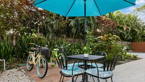 Een terras buiten met een tafel, stoelen, een blauwe parasol en fietsen.