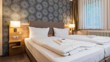 Ein Hotelzimmer mit zwei Betten, einem Holzkopfende, strukturiertem Wandpapier und einem Fenster mit Vorhängen.