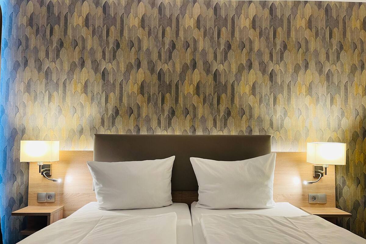 A hotel room with a large bed, two bedside lamps, and a patterned wallpaper.