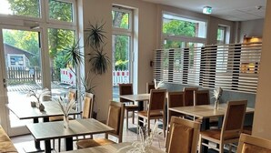 A restaurant with wooden tables and chairs, large windows, and a view of the outside.