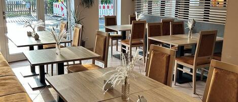 A restaurant with wooden tables and chairs, large windows, and a view of the outside.