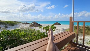 A wooden deck with a view of a beach and thatched umbrellas. - Luxury beach villa in paradise. (Treasure Cay)