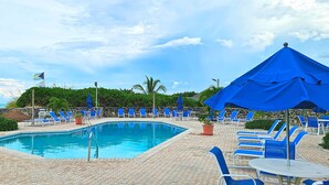 A swimming pool with blue lounge chairs and umbrellas, surrounded by a stone wall and greenery. - Luxury beach villa in paradise. (Treasure Cay)