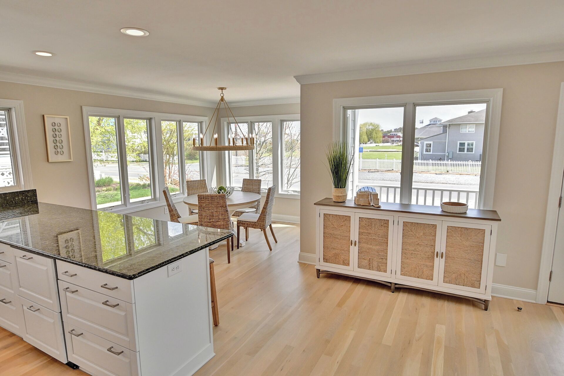 A spacious kitchen with a large island, white cabinetry, and a view of the outside through large windows.