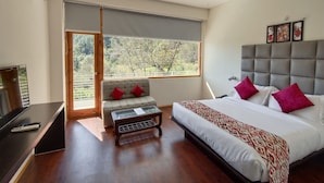 Une chambre à coucher avec un lit, un canapé, une petite table et une fenêtre donnant sur des arbres.
