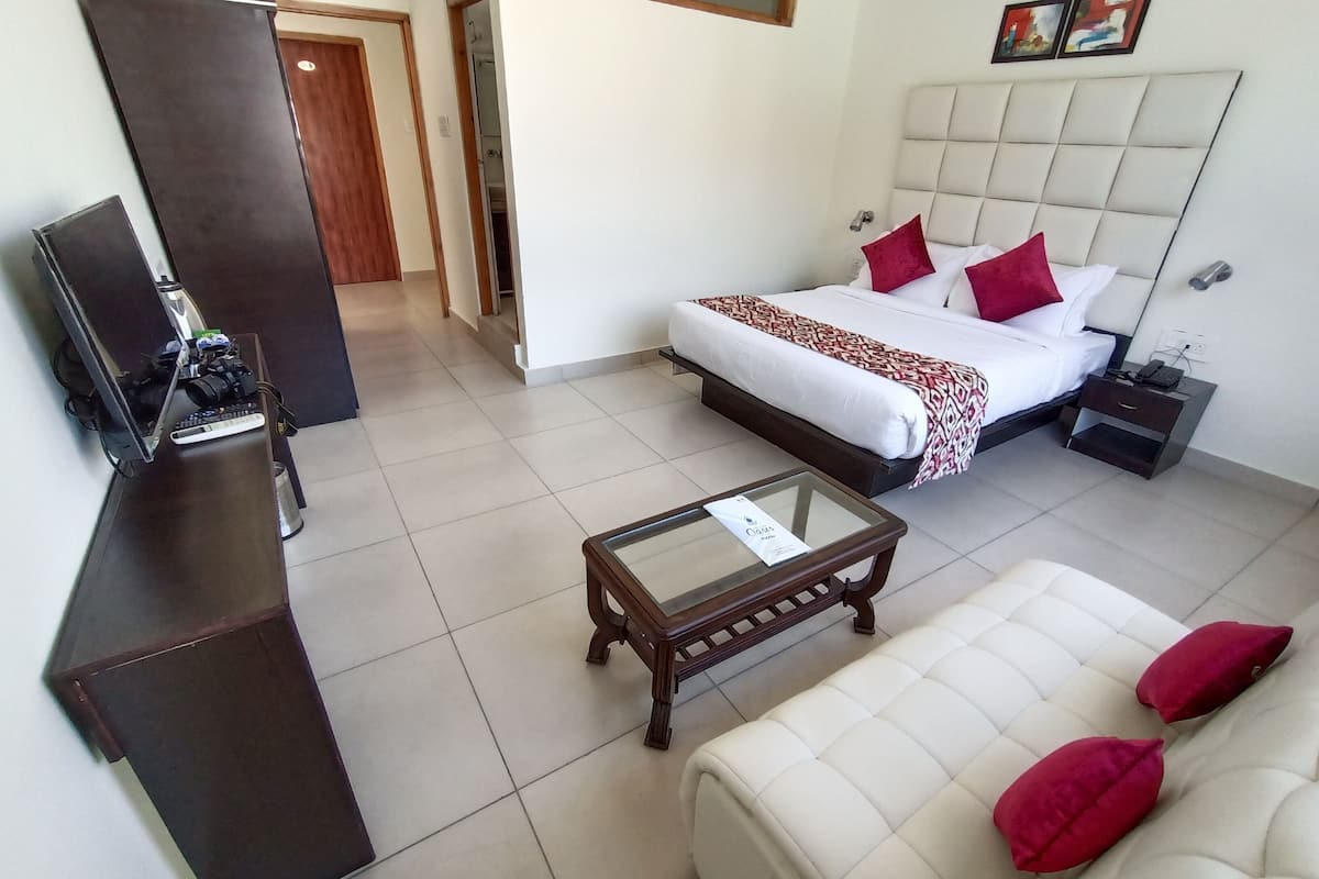 A hotel room with a bed, a sofa, a desk with a computer, and a nightstand.