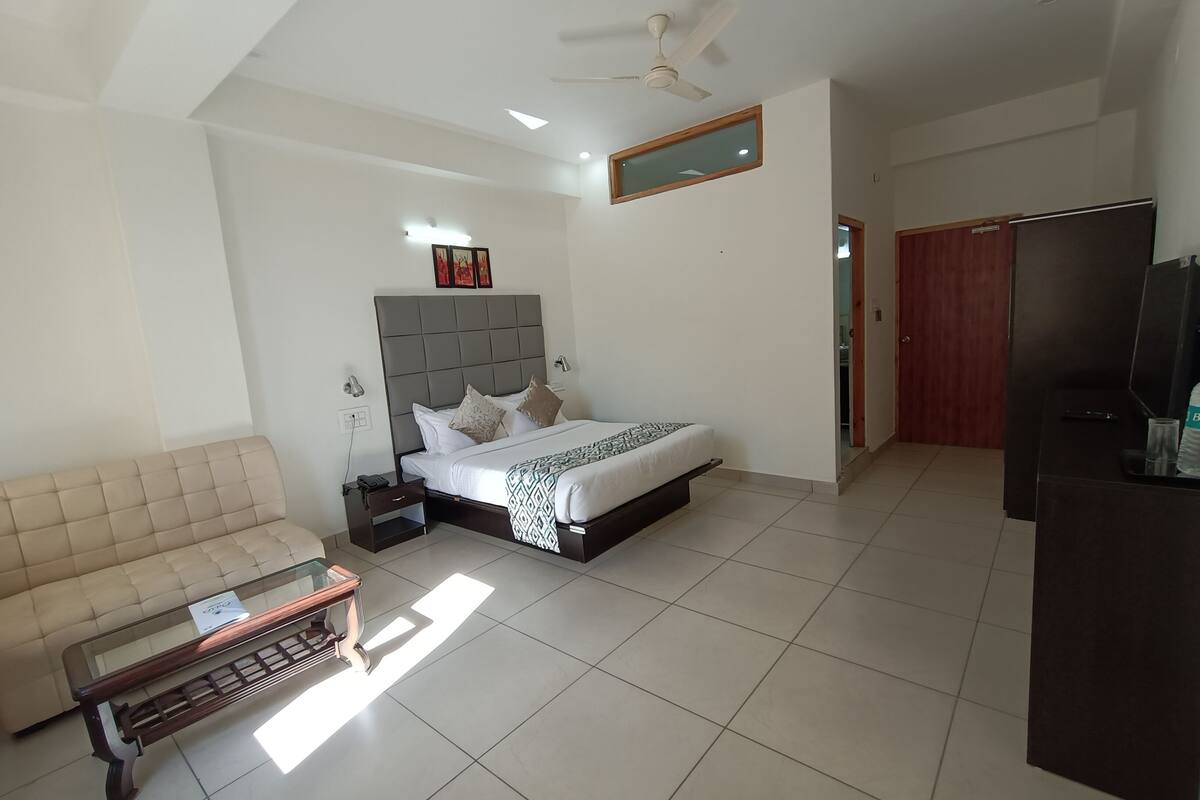 A modern hotel room with a bed, a sofa, a TV, and a ceiling fan.