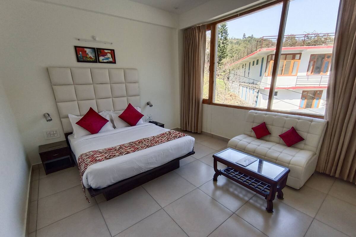 A hotel room with a large bed, a sofa, a small table, and a window with a view of buildings.