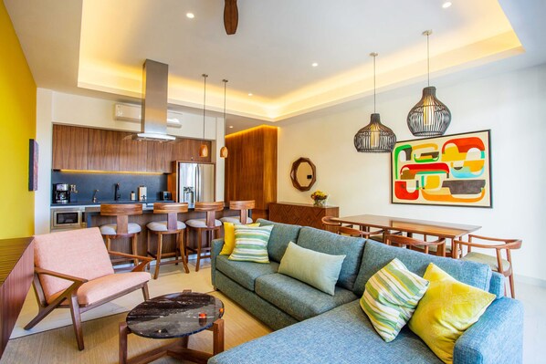 A modern living room with a sofa, armchairs, and a coffee table. There is a kitchen area with a dining set and a bar. - Modern Luxury 2BR in Romantic Zone (Puerto Vallarta)