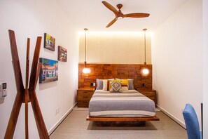 A bedroom with a wooden headboard, a bed with a gray and white striped bedspread, two bedside tables, and a ceiling fan. - Modern Luxury 2BR in Romantic Zone (Puerto Vallarta)
