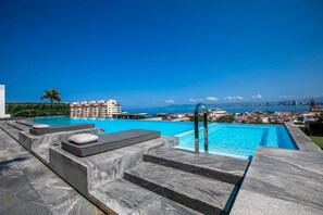 A swimming pool with steps leading down to the water, surrounded by a cityscape and a clear blue sky. - Modern Luxury 2BR in Romantic Zone (Puerto Vallarta)