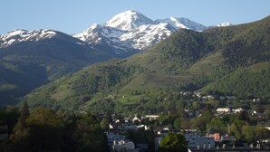A mountain with snow-capped peaks, a town with houses, and lush green hills. - Krys Chambre vue sur les Pyrenees et le pis du Midi (Bagnères-de-Bigorre)