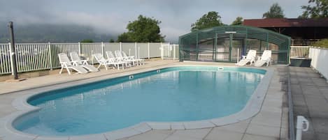 A swimming pool with white lounge chairs and a glass-enclosed structure.