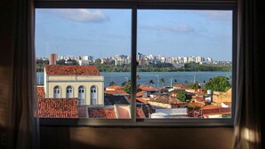 A view through a window of a cityscape with a body of water, buildings, and a prominent structure with a red-tiled roof. - Hostel da Fonte (São Luís)