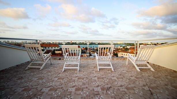 A rooftop terrace with three white chairs and a patterned floor, overlooking a cityscape. - Hostel da Fonte (São Luís)