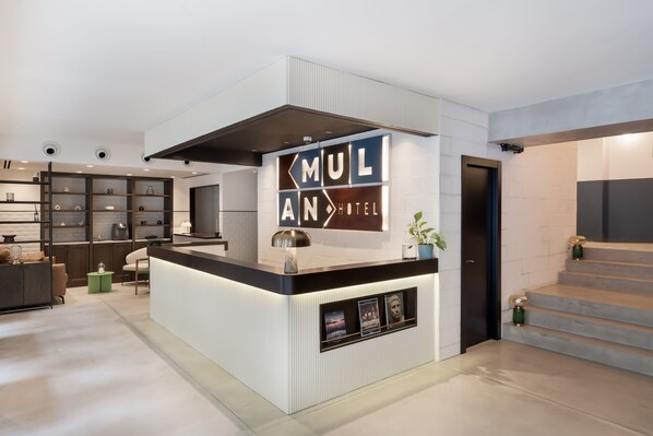 A hotel reception area with a modern design, featuring a reception desk, a large sign for 'MULAN HOTEL', and a staircase leading to the upper floors. - Mulan TLV Hotel (Tel Aviv)