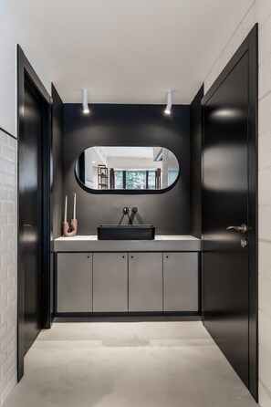 A modern bathroom with a black vanity, a round mirror, and a white sink. - Mulan TLV Hotel (Tel Aviv)