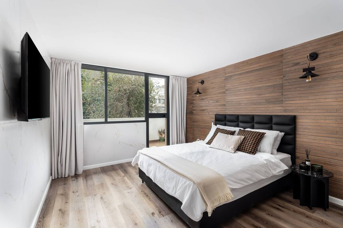 A bedroom with a large bed, a TV mounted on the wall, and a wooden panel wall.