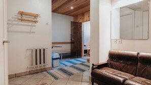 Una habitación con sofá de cuero marrón, techo de madera, radiador, alfombra azul y blanca a rayas, y banco de madera.