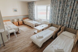 Habitación de hotel con tres camas individuales, un escritorio con silla, una mesita y una ventana con cortinas.