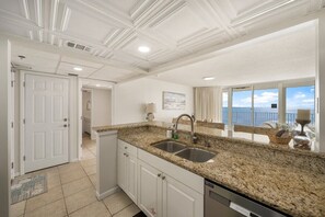 A kitchen with granite countertops, a double sink, white cabinets, and a view of the ocean through large windows.