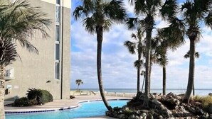 Una piscina con agua cristalina azul, rodeada de palmeras y un edificio de diseño moderno.