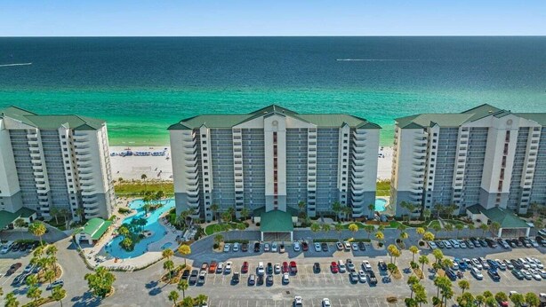 A beachfront hotel with multiple high-rise buildings, a parking lot, and a swimming pool.