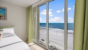 A bedroom with a large sliding glass door leading to a beach view.