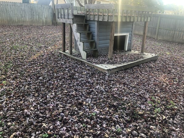 A wooden playhouse with a slide and stairs, surrounded by a ground covered with dry leaves. - Fayetteville Home Getaway near UofA (Fayetteville)