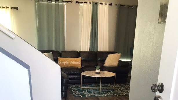 A living room with a dark wood floor, a black leather sofa, a round coffee table, and a green patterned rug.