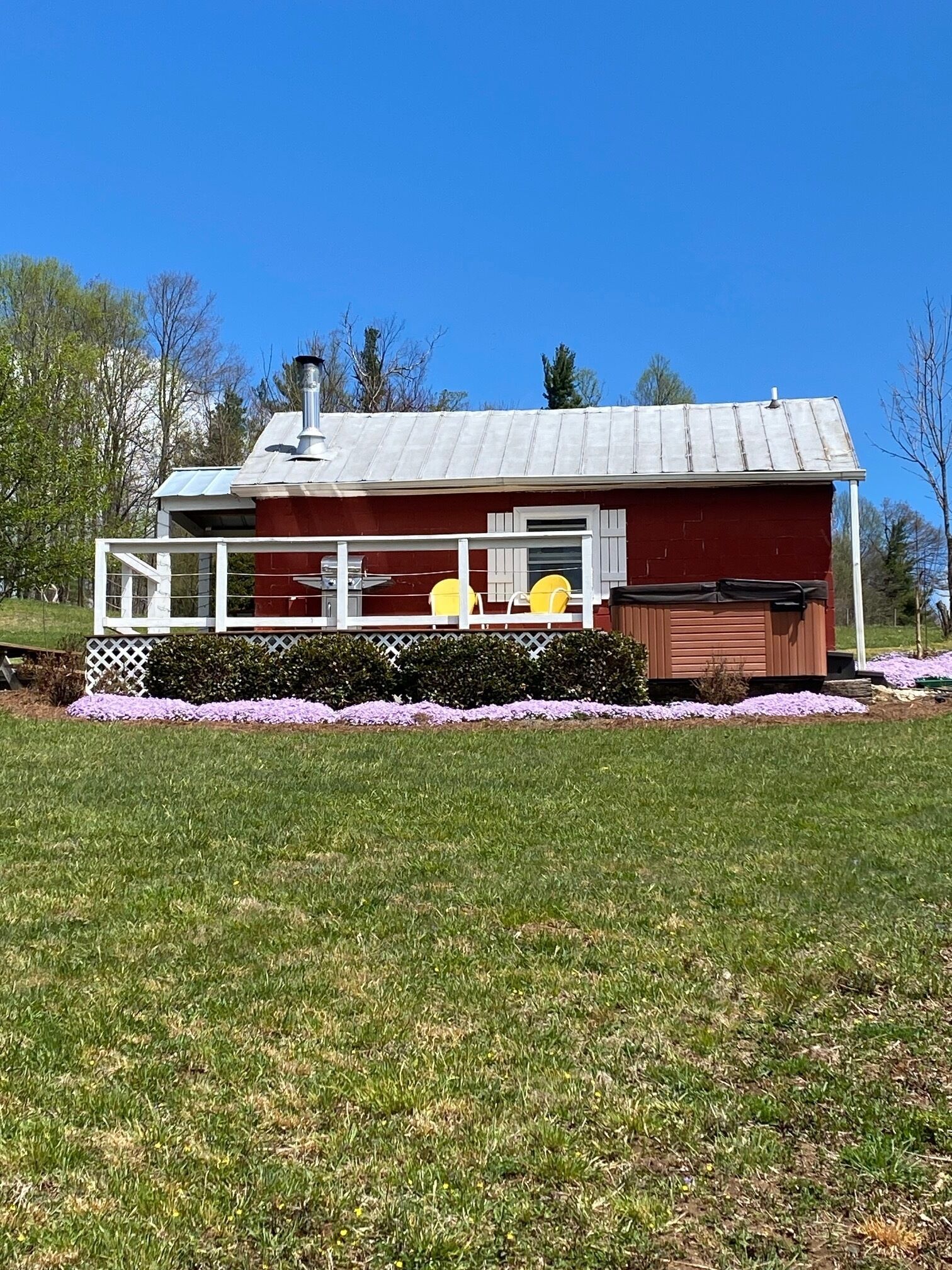 A red building with a white porch, a chimney, and a small shed.