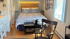 Un dormitorio con cama, cabecera de madera, escritorio, silla, ventana con cortinas y estante fijado a la pared.