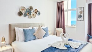 A neatly made bed with a blue blanket and white swan-shaped towels, a bedside lamp, and a wall art piece above the bed. - Apartment Praia Rocha Balcony Amazing (Portimão)