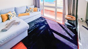 A modern living room with a sofa, a coffee table, and a view of the sea through large windows. - Apartment Praia Rocha Balcony Amazing (Portimão)