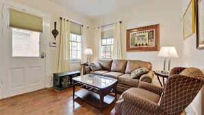Ein Wohnzimmer mit einem braunen Ledersofa, einem Glastisch, einem gemusterten Sessel und einer Zierkommode.