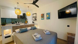 Una habitación de hotel moderna con cama, mesitas de noche, televisor y zona de cocina.