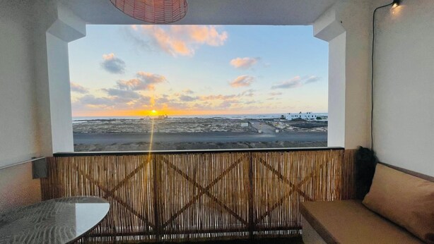Una habitación con vista a un atardecer sobre la playa, un separador de madera y una pequeña mesa.
