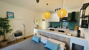 Una cocina moderna con encimera blanca, salpicadero verde y campana extractora negra. Hay una zona de comedor con un banco y dos cojines azules.