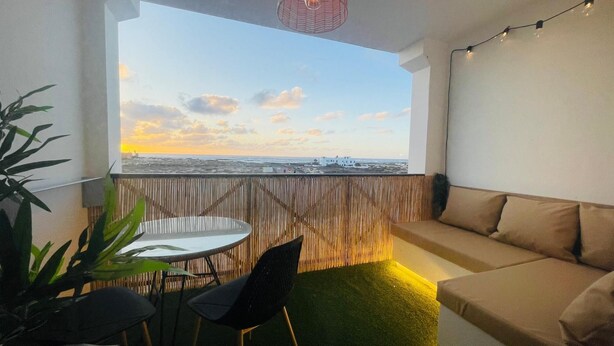 Ein Balkon mit Meerblick, ein runder Tisch mit Stühlen und eine Couch.