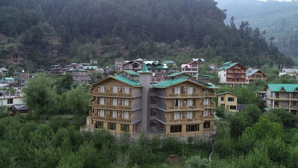 A multi-story building with balconies, surrounded by greenery and other buildings. - Gezellig Inn - Golden Apple (Manali)