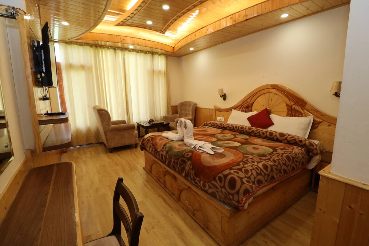 A hotel room with a wooden bed, a chair, a desk, and a television.