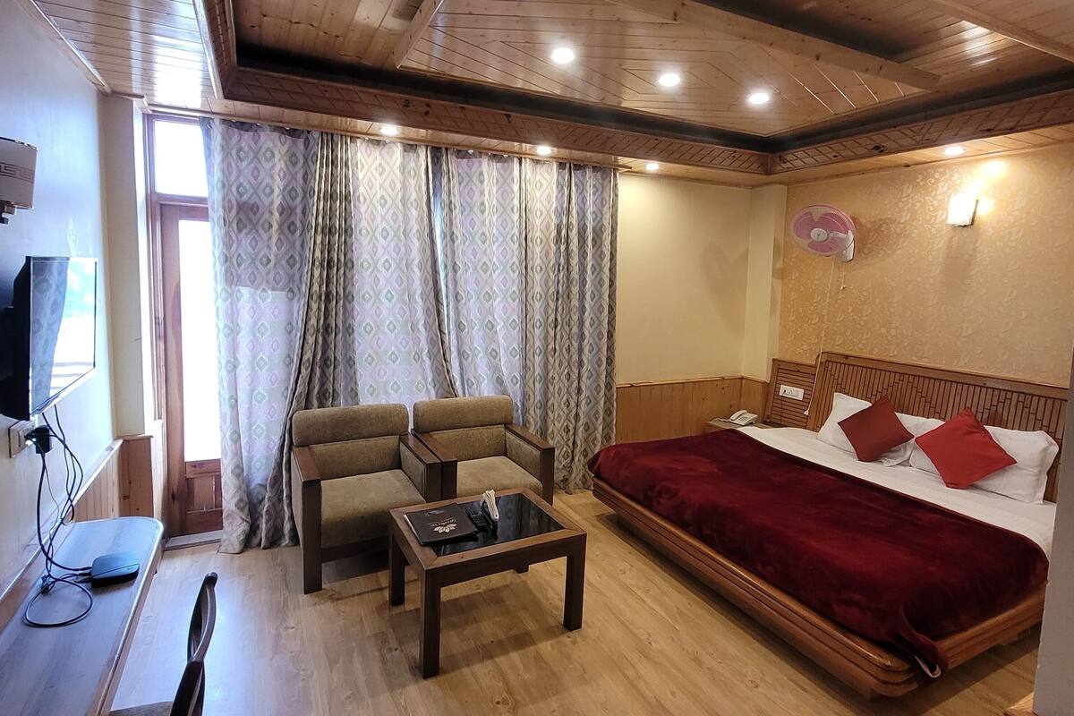 A cozy room with a wooden ceiling, a bed with red bedding, a sofa, a small table, and a TV on a wooden stand.