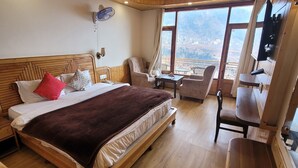 A hotel room with a large bed, a desk, a chair, and a view of the mountains. - Gezellig Inn - Golden Apple (Manali)
