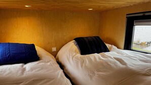 Two beds with white bedding and dark blue pillows in a room with wooden walls and a window.