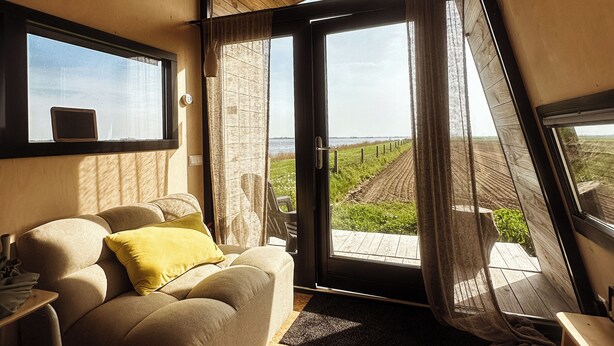 A modern bedroom with a large window, a sofa, and a wooden floor.