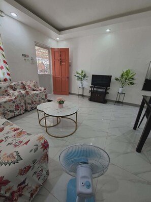 A living room with a sofa, a coffee table, a TV, and two potted plants. - Beautiful Compostela 2 Story Townhouse with Patio  (Compostela)