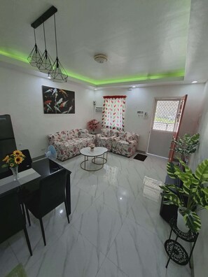 A living room with a sofa set, a dining table with chairs, a coffee table, and a TV. - Beautiful Compostela 2 Story Townhouse with Patio  (Compostela)