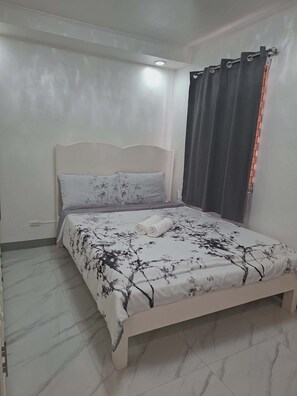 A bedroom with a bed, a headboard, a window with curtains, and a light fixture. - Beautiful Compostela 2 Story Townhouse with Patio  (Compostela)